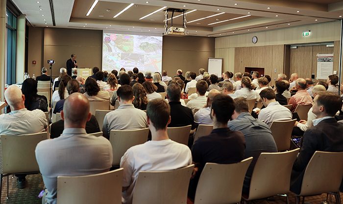 Publikum in Vortragssaal mit Leinwand und Vortragendem
